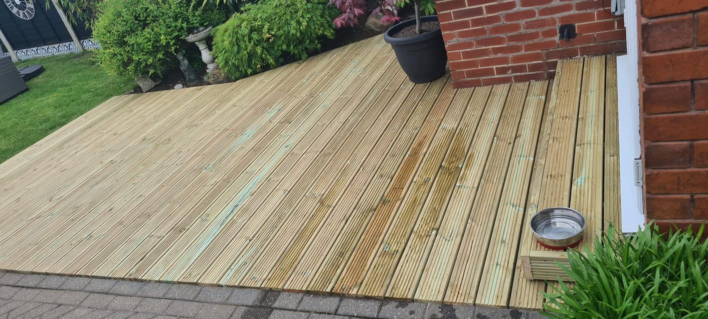 Wide garden decking next to lawn and brick wall